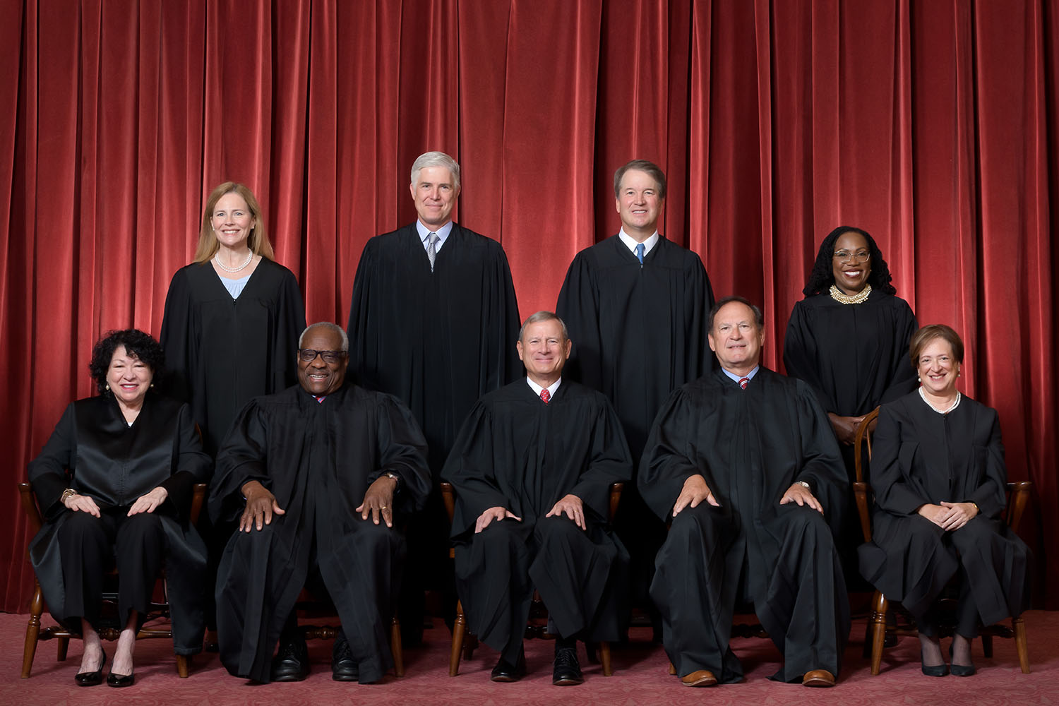 Formal group photograph of the Supreme Court as it was been comprised on June 30, 2022 after Justice Ketanji Brown Jackson joined the Court. The Justices are posed in front of red velvet drapes and arranged by seniority, with five seated and four standing. Credit: Fred Schilling, Collection of the Supreme Court of the United States